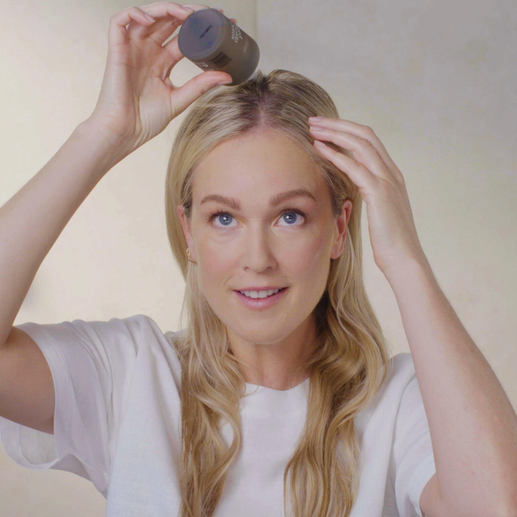 Woman applying scalp product to her parted hair roots.