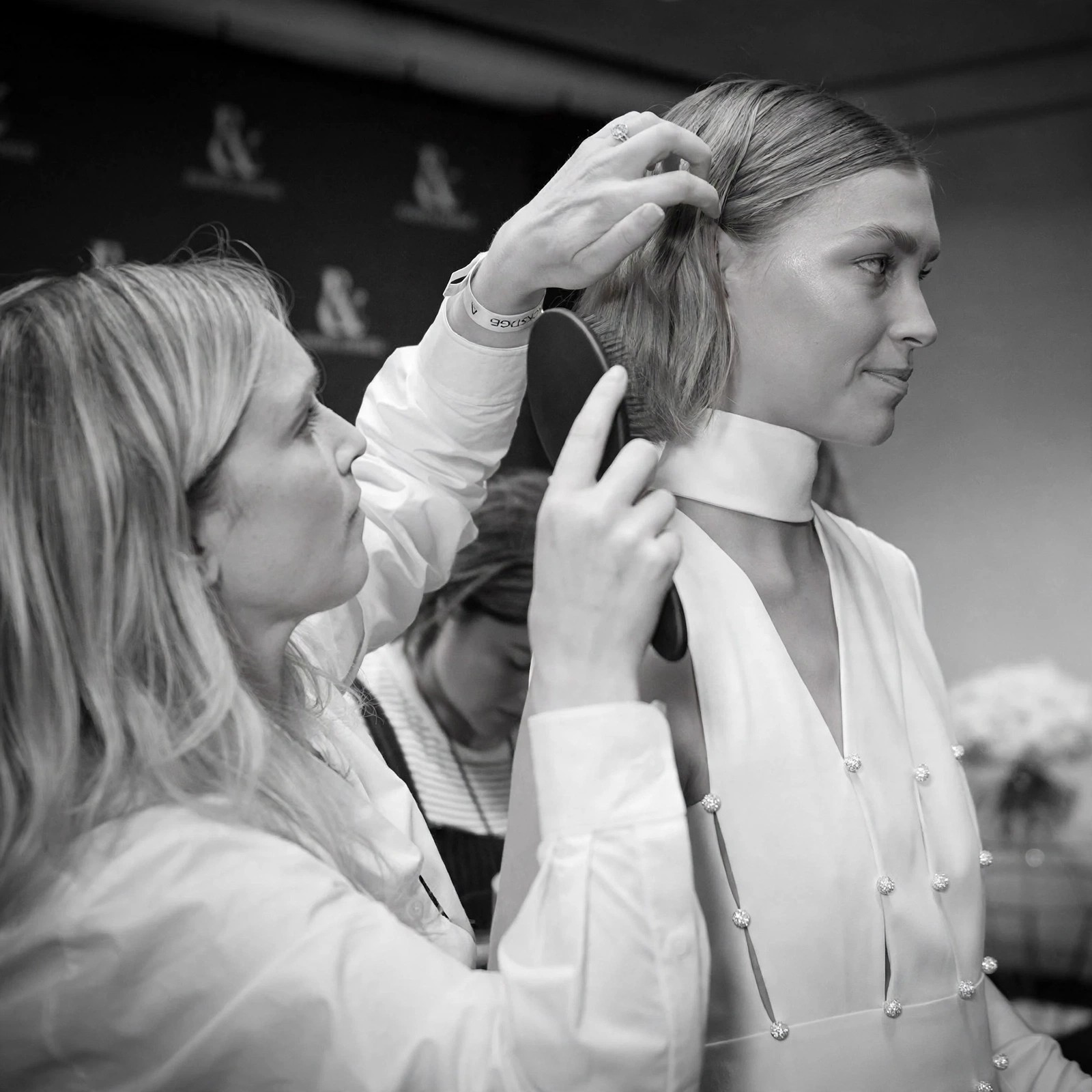 Hairstylist brushing a model's hair backstage in black and white.