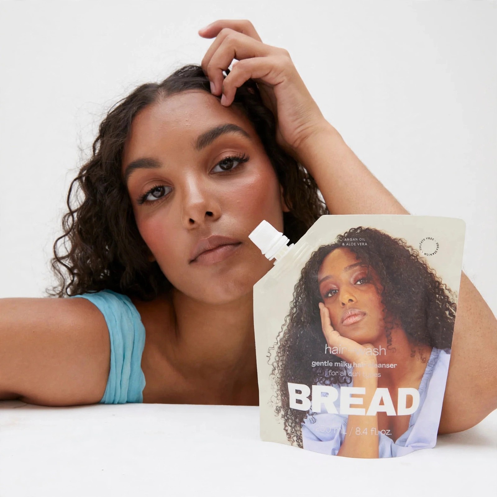 Woman with curly hair posing beside Bread hair wash pouch.