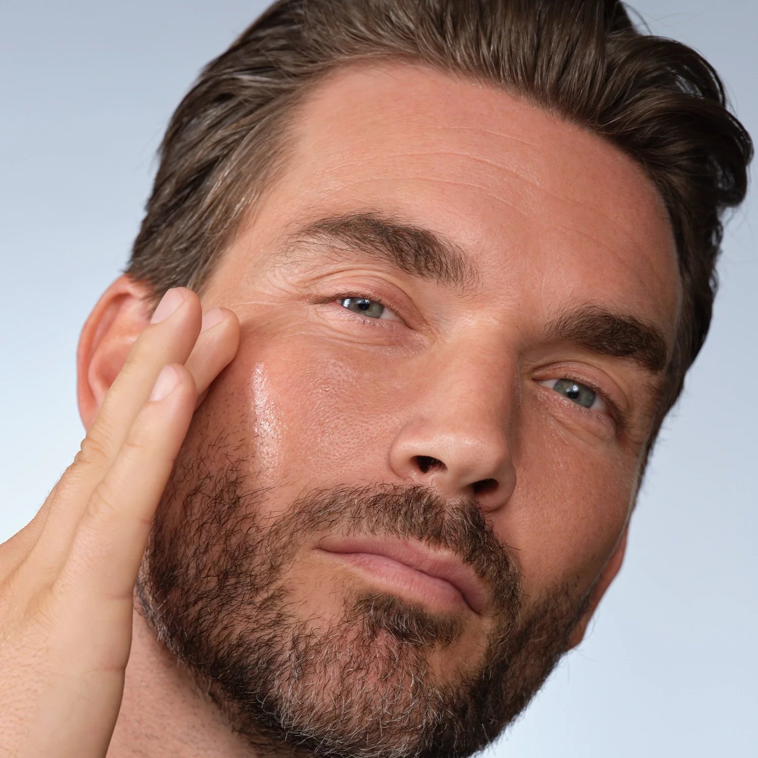 Close view of a model smoothing serum on his face.