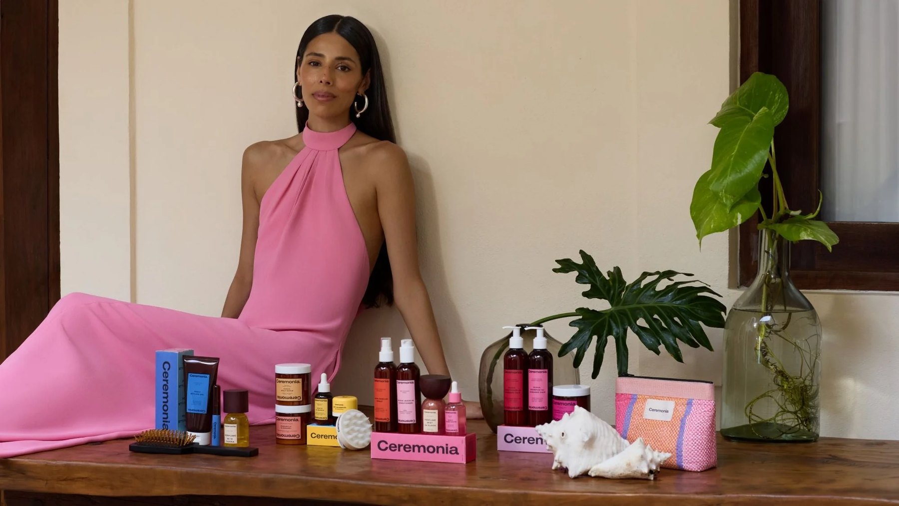 Woman in pink dress beside table of Ceremonia products.