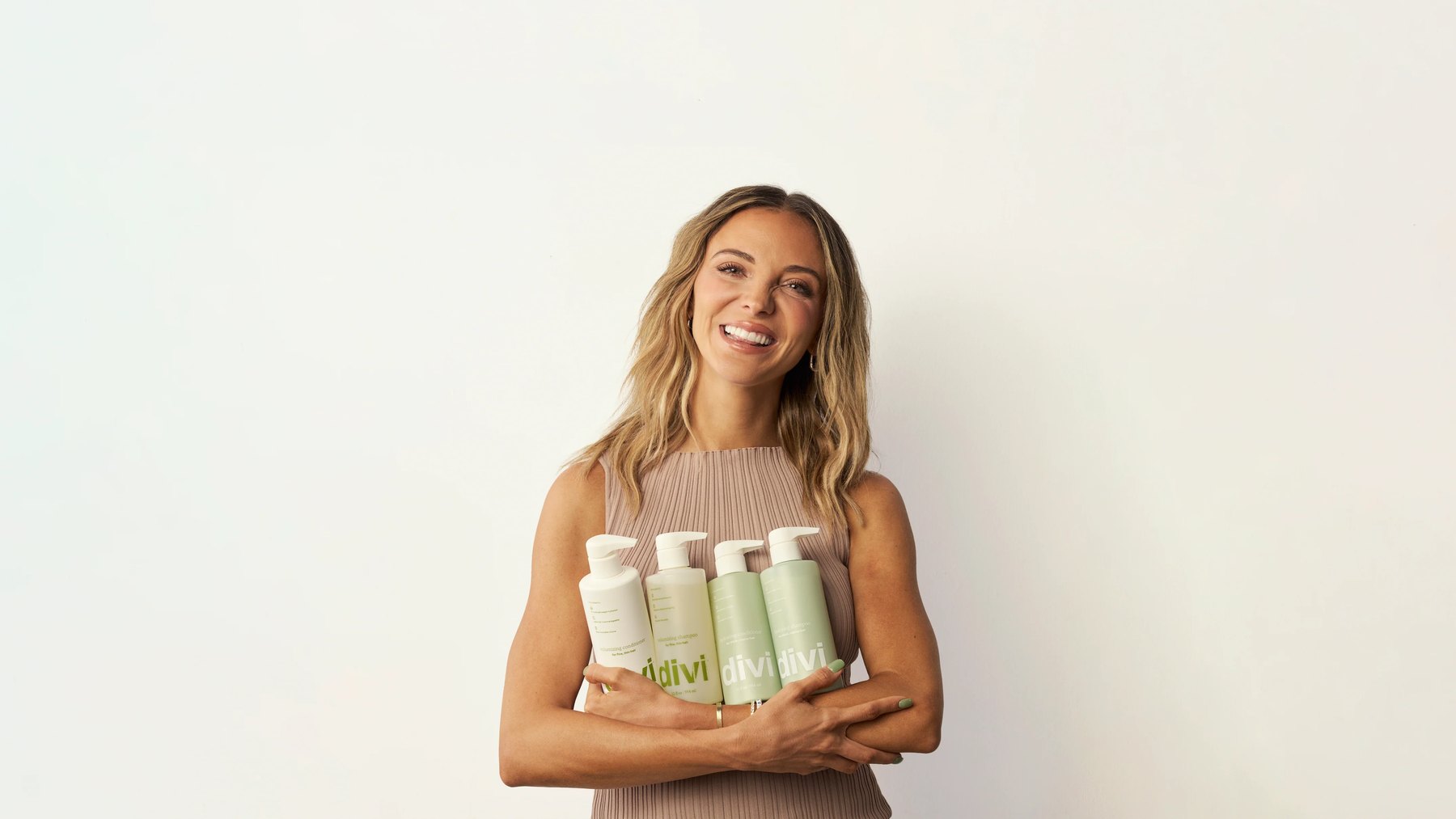 Dani Austin smiles holding four Divi bottles against white wall.