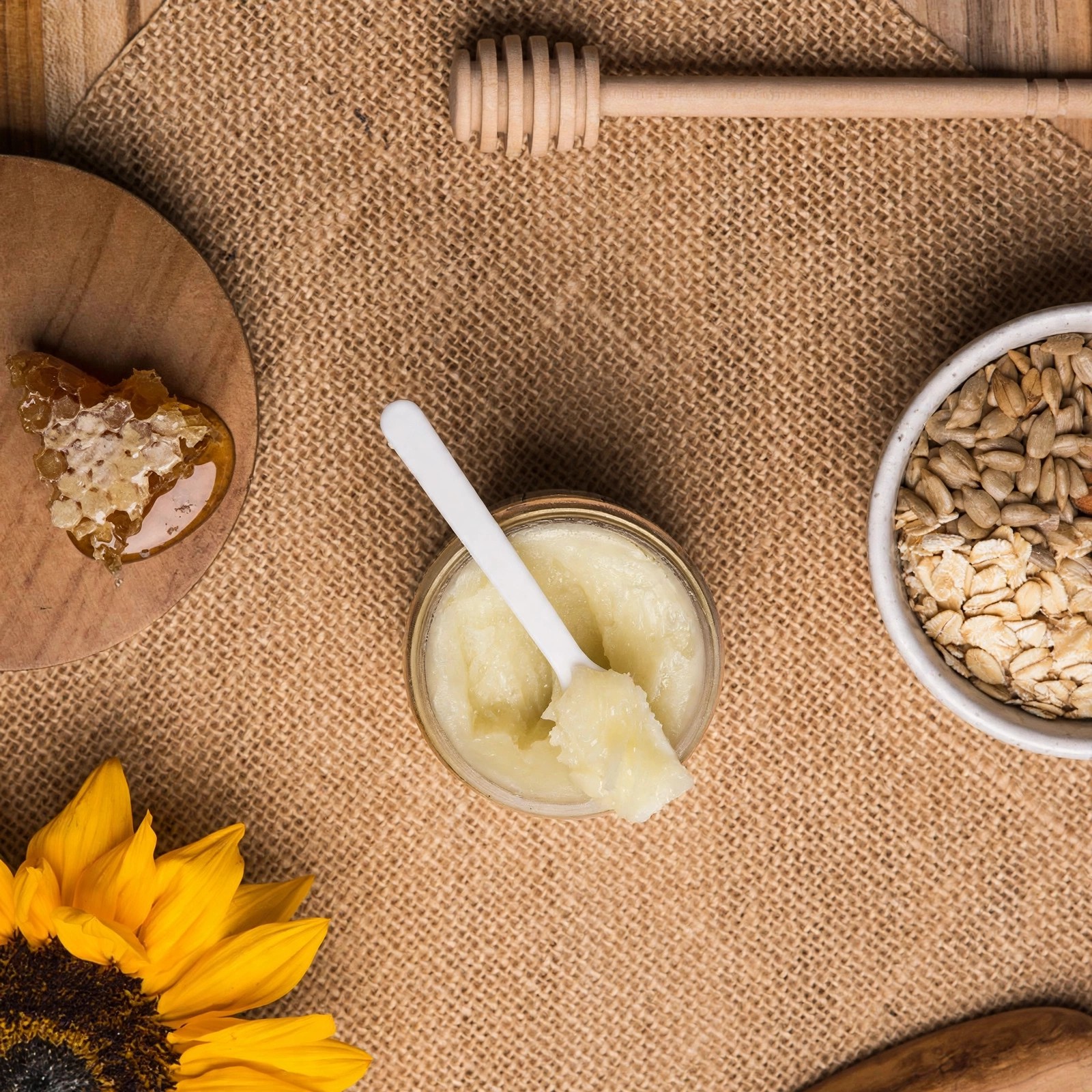 Jar of balm beside oats, honeycomb and dipper from above.