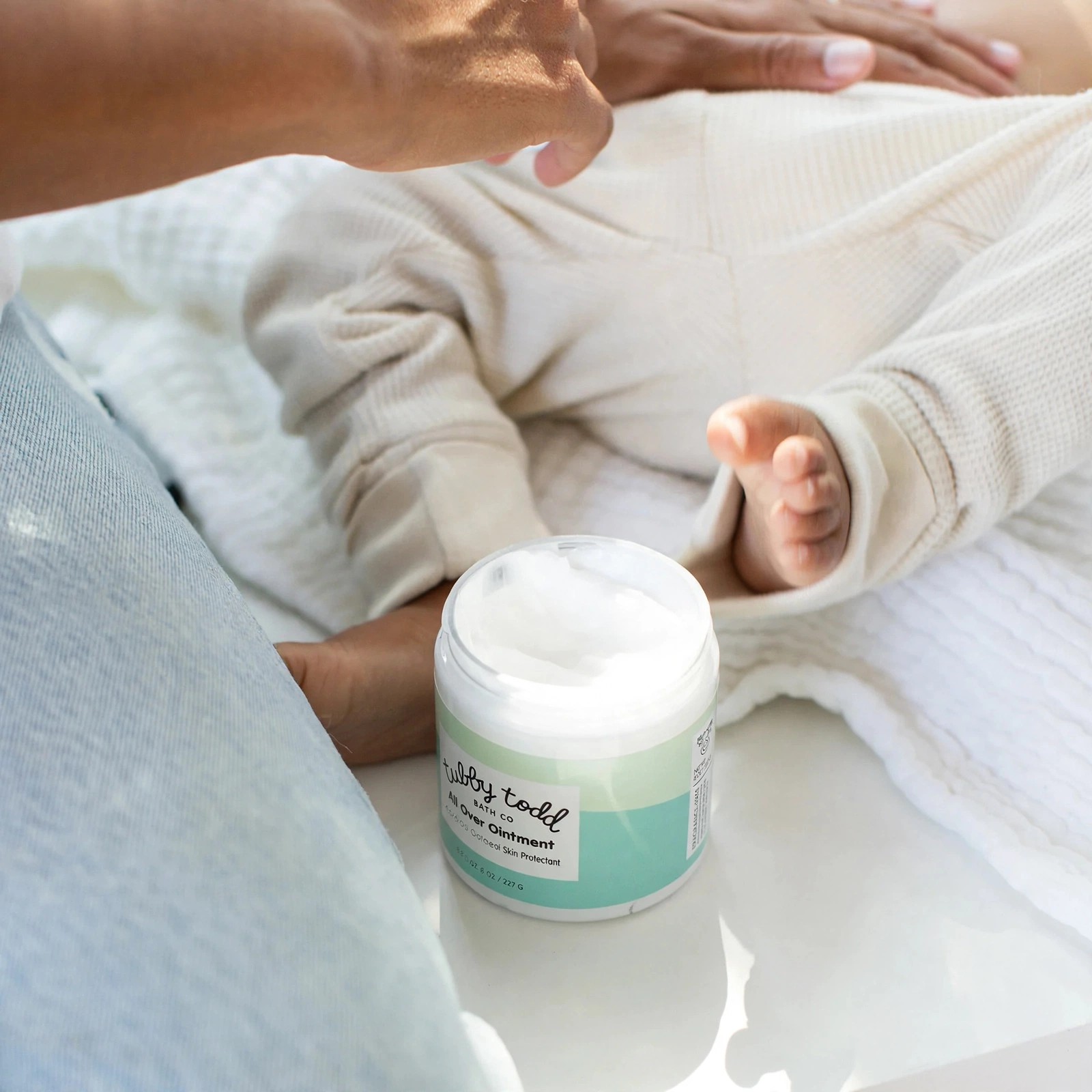 Hands near an infant with a jar of balm.
