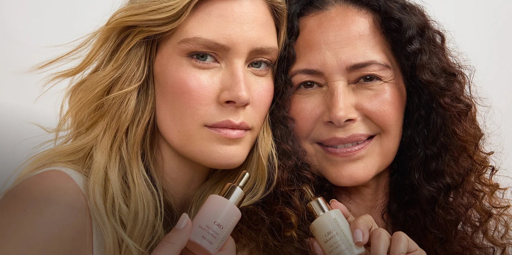 Two women with long hair holding Vegamour serum bottles.